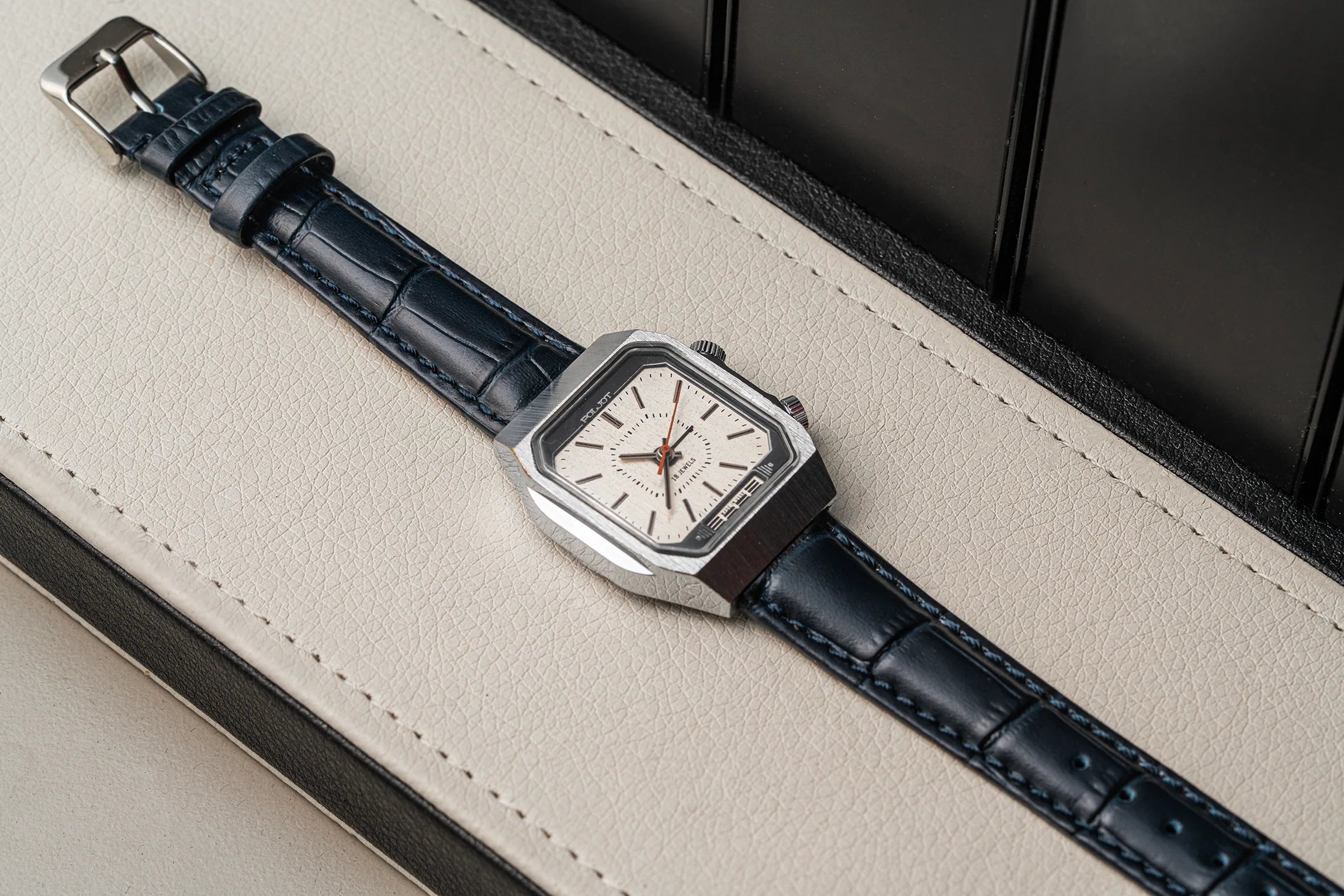 A rectangular silver-tone wristwatch Poljot Alarm, Cal. 2612.1 with a white dial and a dark navy blue alligator-embossed leather strap, resting diagonally on a cream-colored textured leather surface.