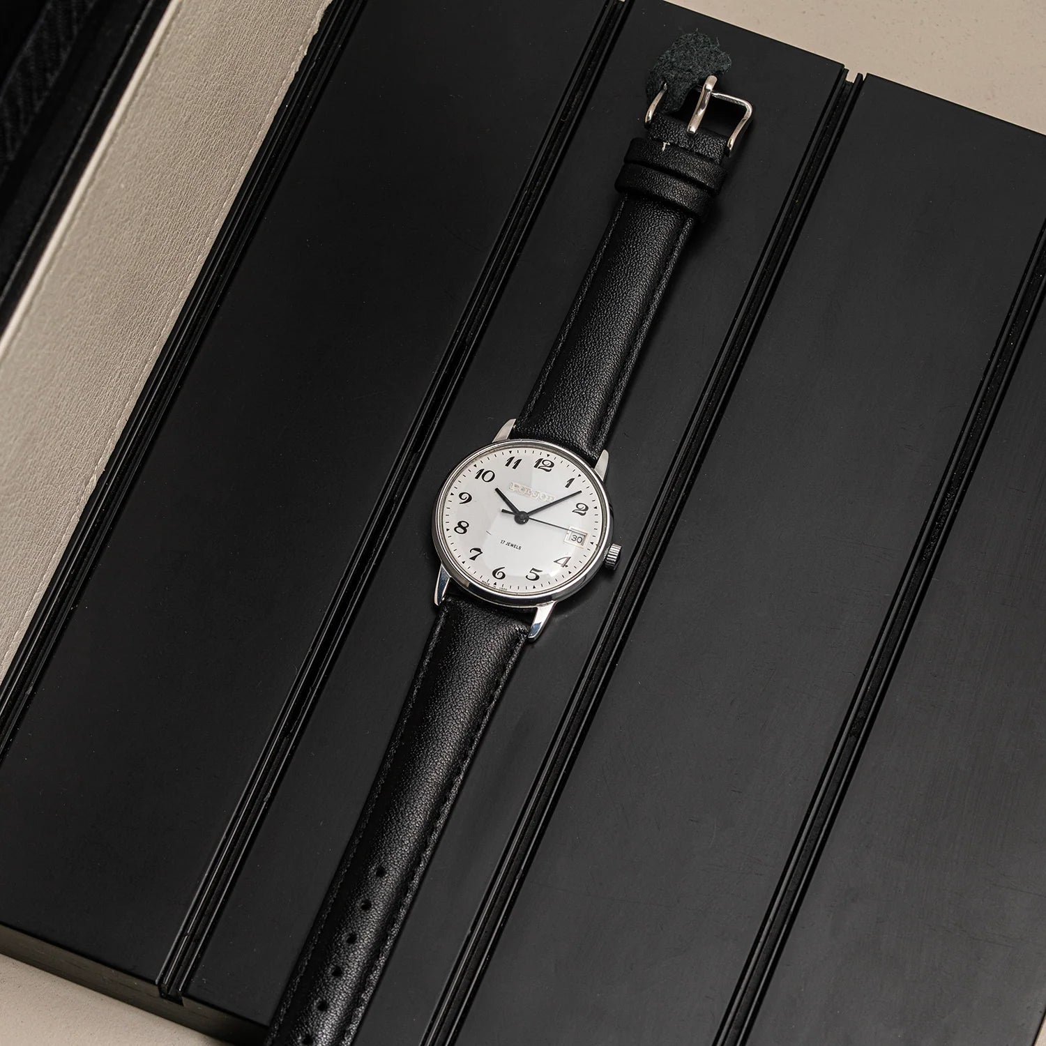 A vintage-style wristwatch Poljot 2614.2H with a white dial and black leather strap, displayed diagonally on a black textured surface.