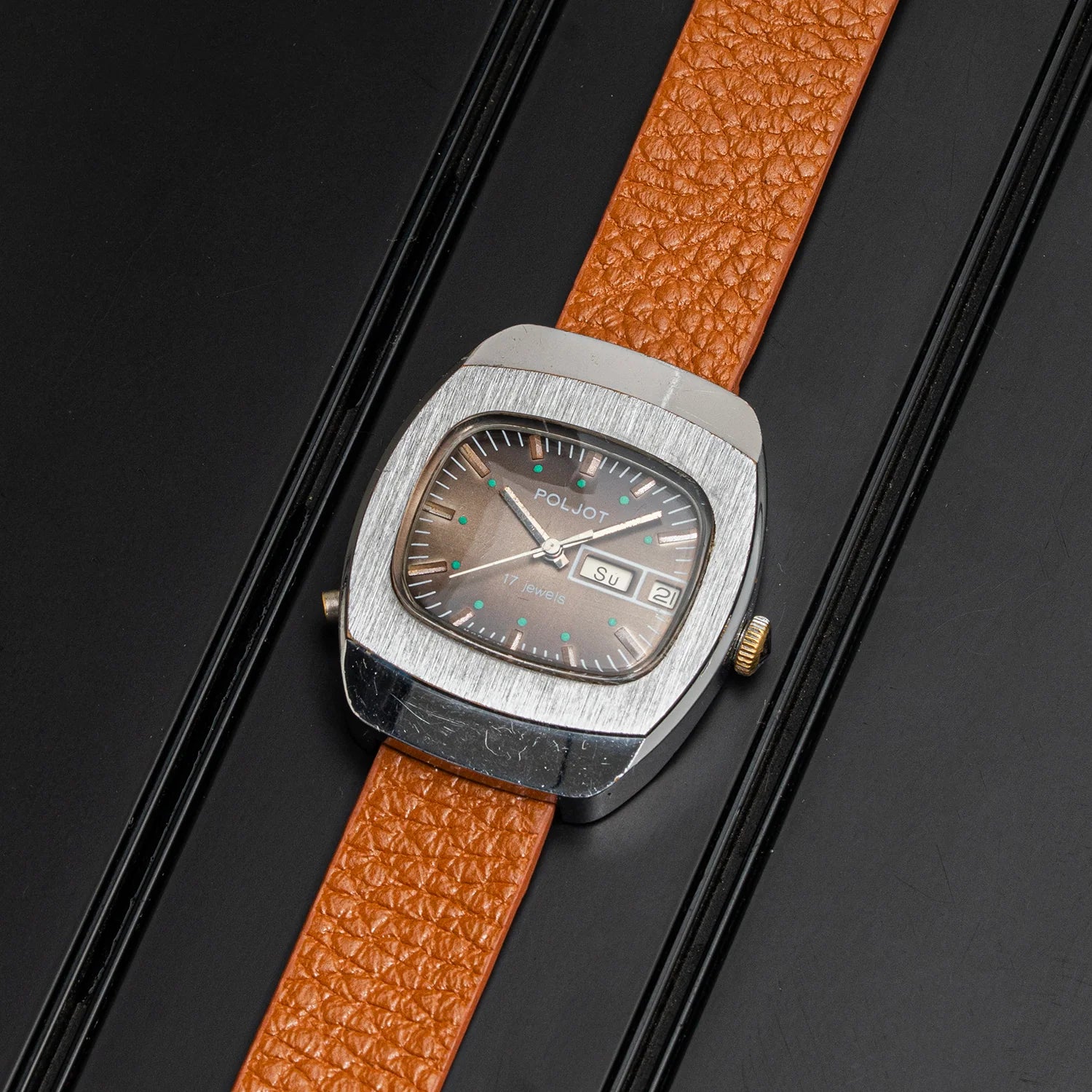 A vintage-style wristwatch Poljot with a brushed silver-tone case, brown dial, and textured orange-brown leather strap, photographed diagonally on a black background.