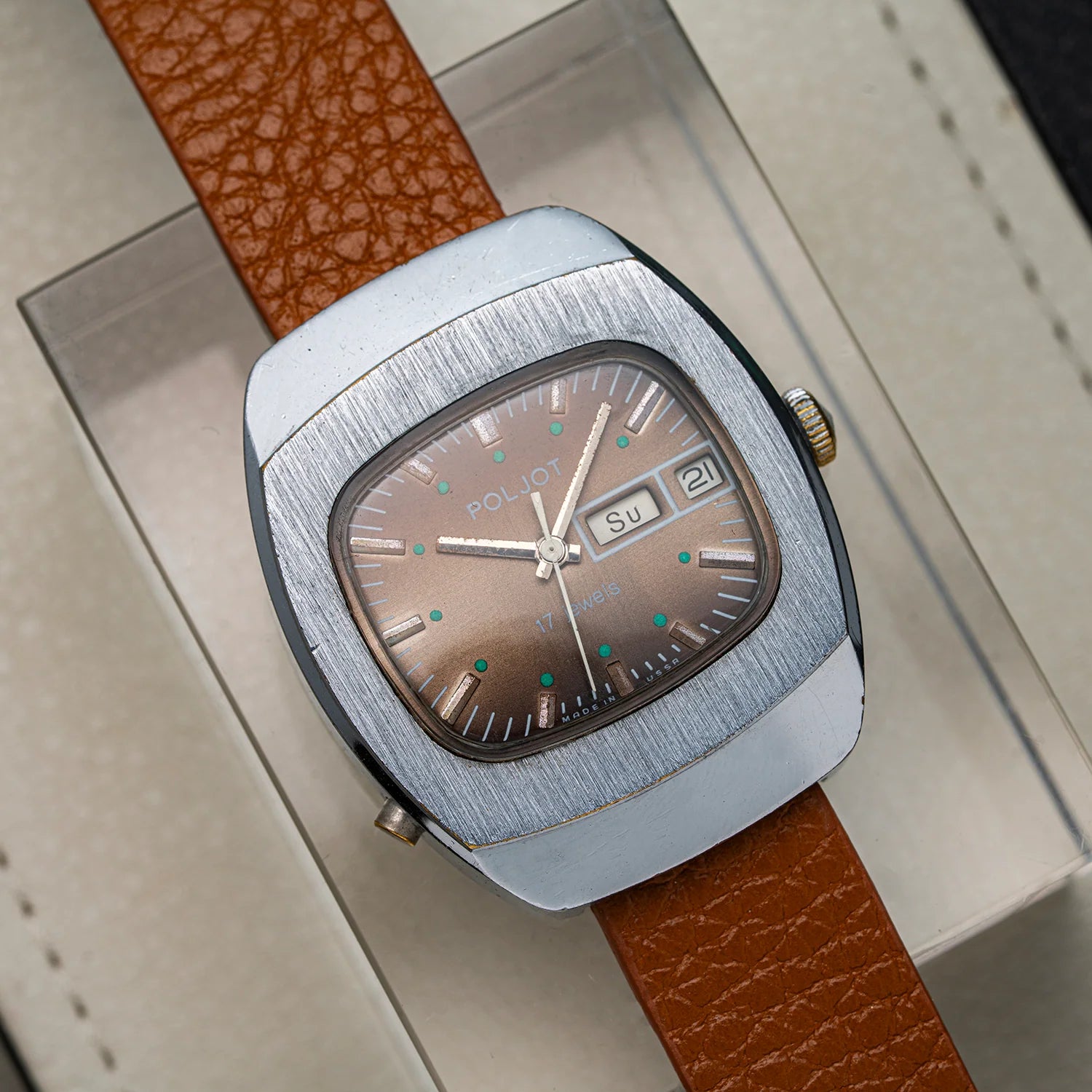 A vintage-style wristwatch Poljot with a brushed silver-tone case, brown dial, and brown textured leather strap, photographed resting on a light-colored surface.