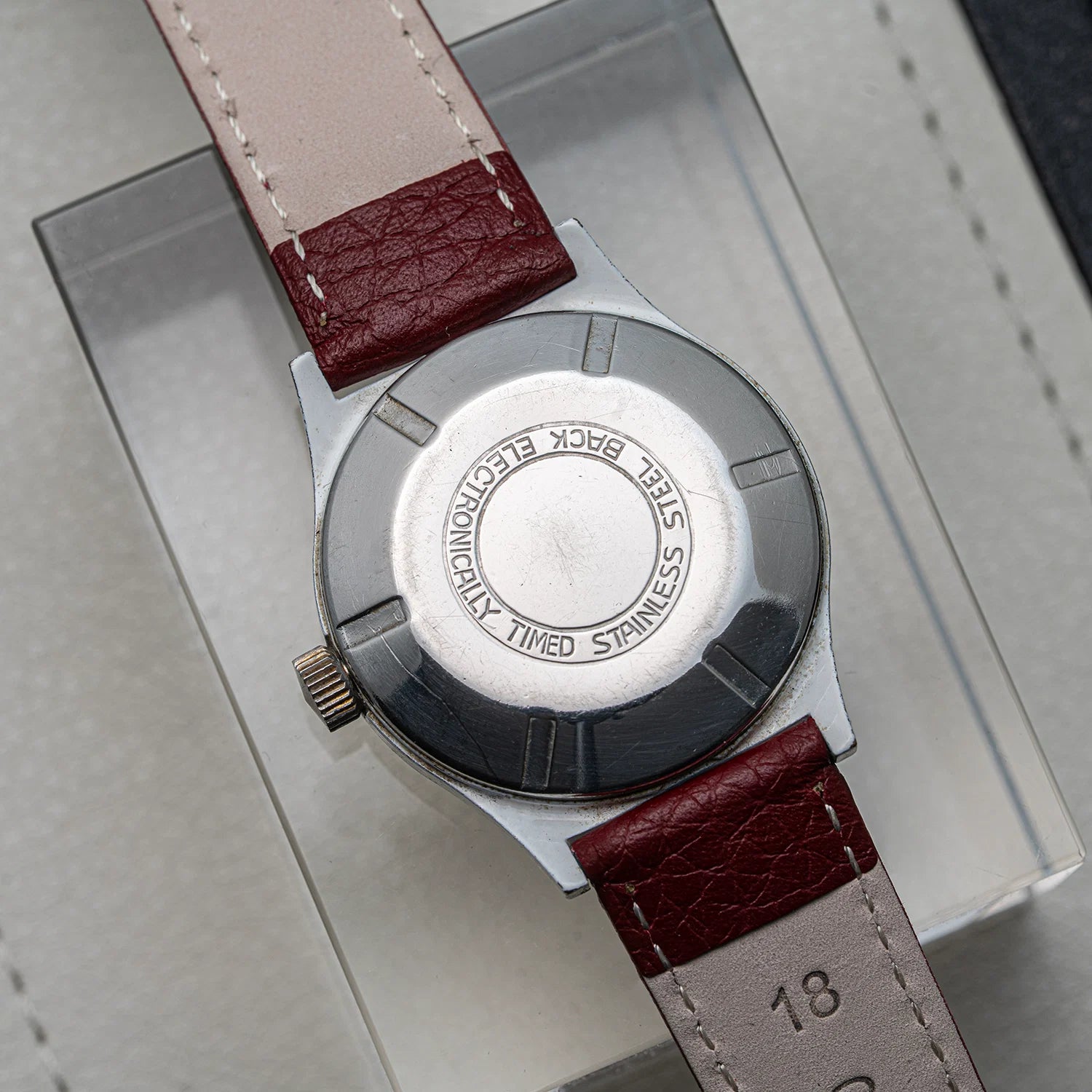 Close-up of the back of a wristwatch  Ruhla, Cal. UMF 24-42with a silver stainless steel case and a reddish-brown leather strap on a light gray surface.
