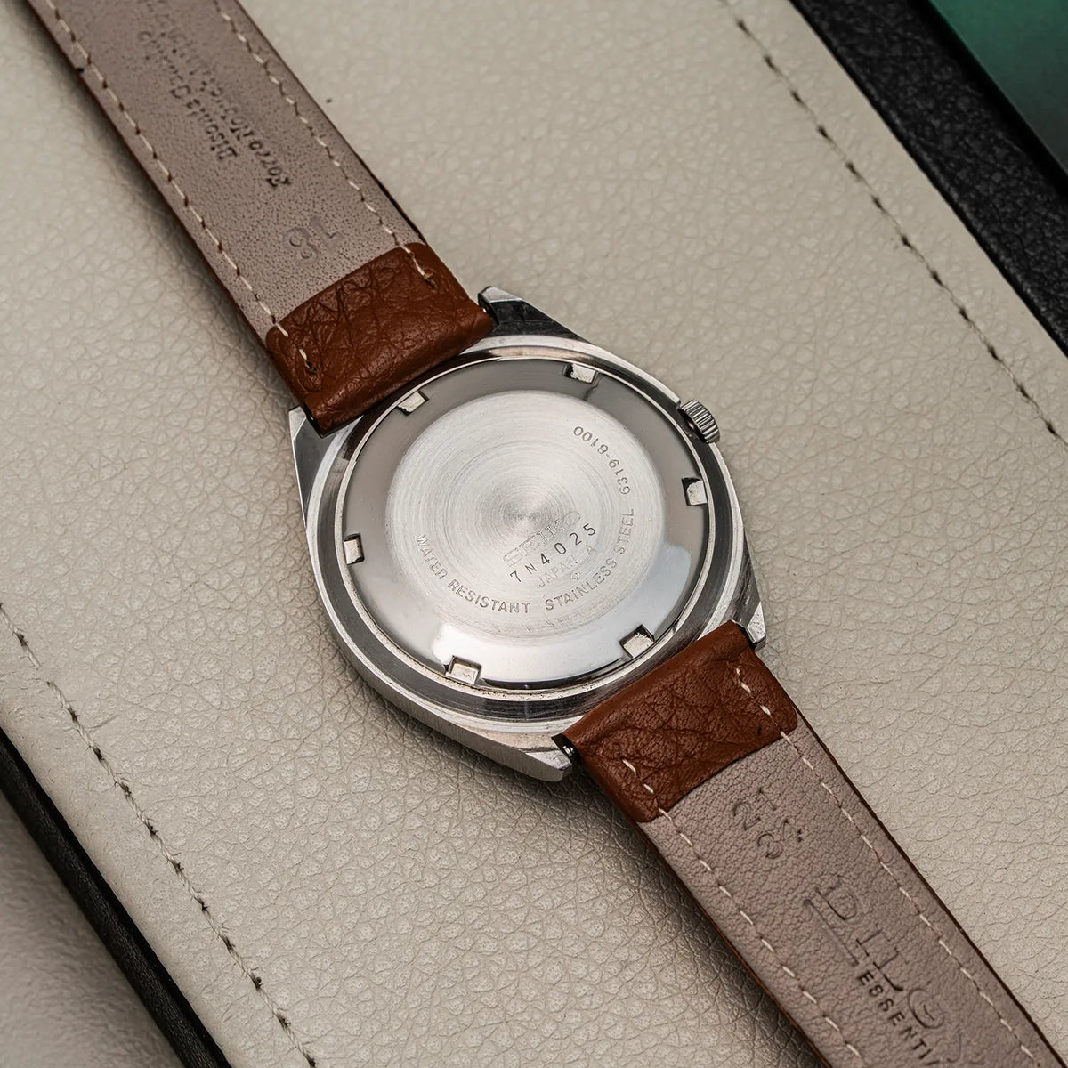Close-up of the back of a wristwatch Seiko 5, Ref. 6319-8100, Cal. 6319, Men’s Automatic, 1977 with a silver stainless steel case and a brown leather strap on a light textured surface.