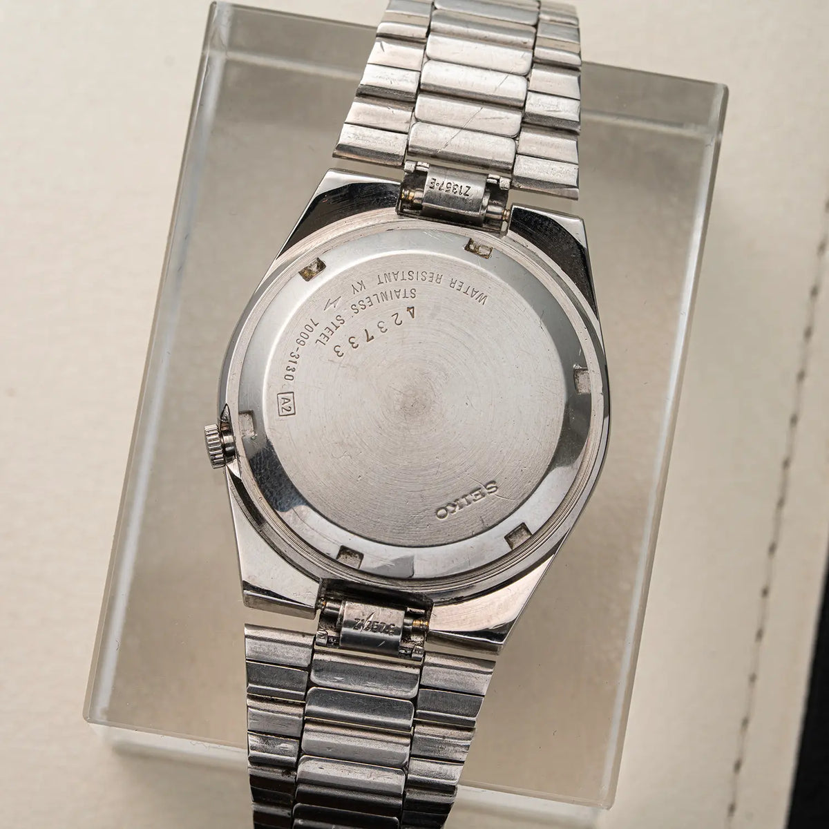 A stainless steel wristwatch Seiko 5, Ref. 7009-3130, Cal. 7009, Men’s Automatic, 1984 shown from the back, mounted on a clear display stand. The silver metal case and link bracelet are visible, with engraved text on the back cover including 'SEIKO'.