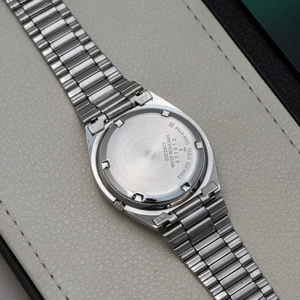 Close-up of the back of a stainless steel wristwatch Seiko 5, Ref. 7009-8750, Cal. 7009, Men’s Automatic, 1984 with a metal link bracelet, resting on a light textured surface.