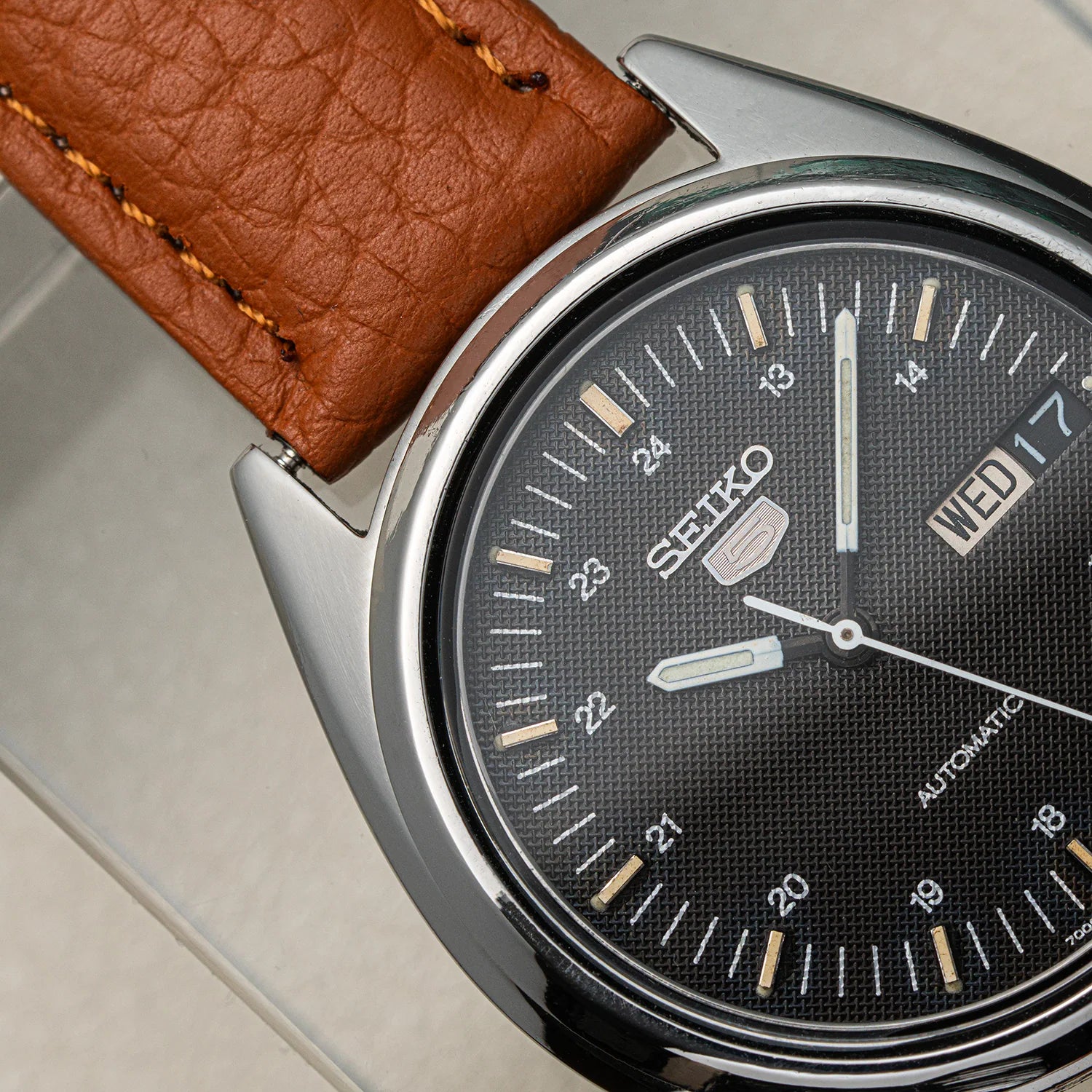 Close-up of a Seiko 5 7009-3040 Automatic watch with a brown leather strap, silver-toned metal case, and a textured black dial with white markings and a day-date window.