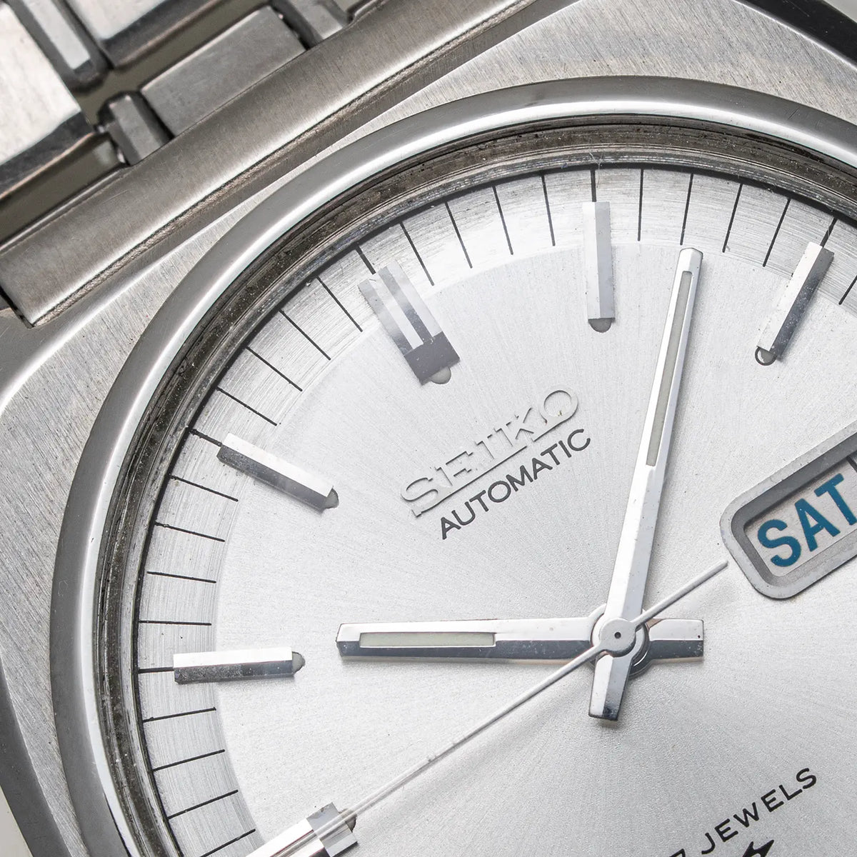 Close-up of a Seiko, Ref. 7009-8100, Cal. 7009, Men’s Automatic, 1977 watch dial and bracelet, showing a brushed silver-toned metal case, silver dial, stick indices, and part of the bracelet.