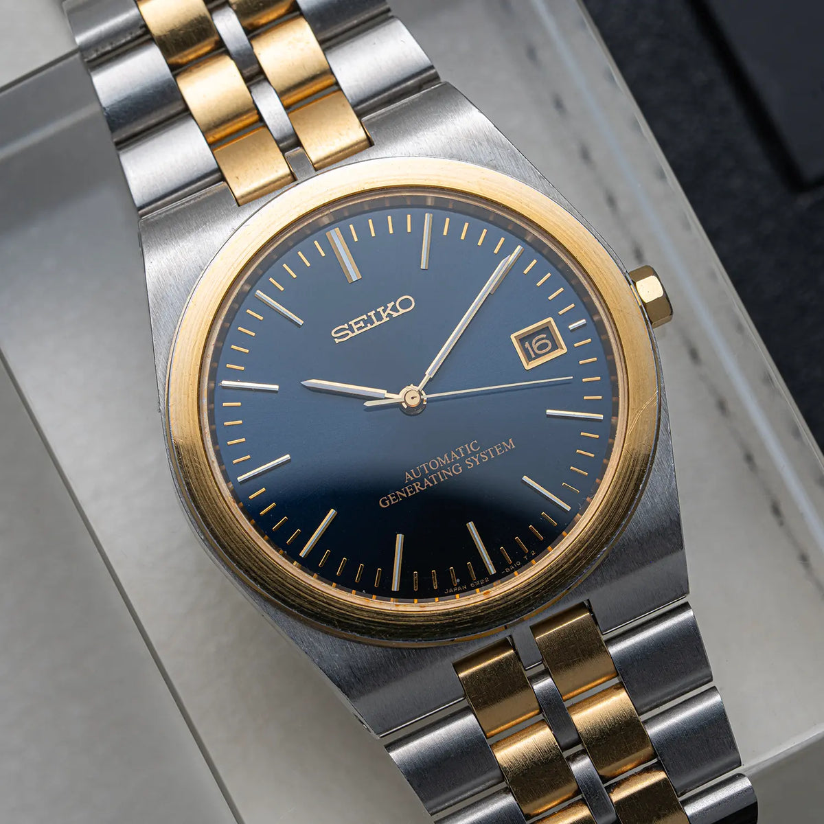 A close-up shot of a Seiko automatic watch with a two-tone silver and gold metal bracelet, a gold bezel, and a dark blue dial.