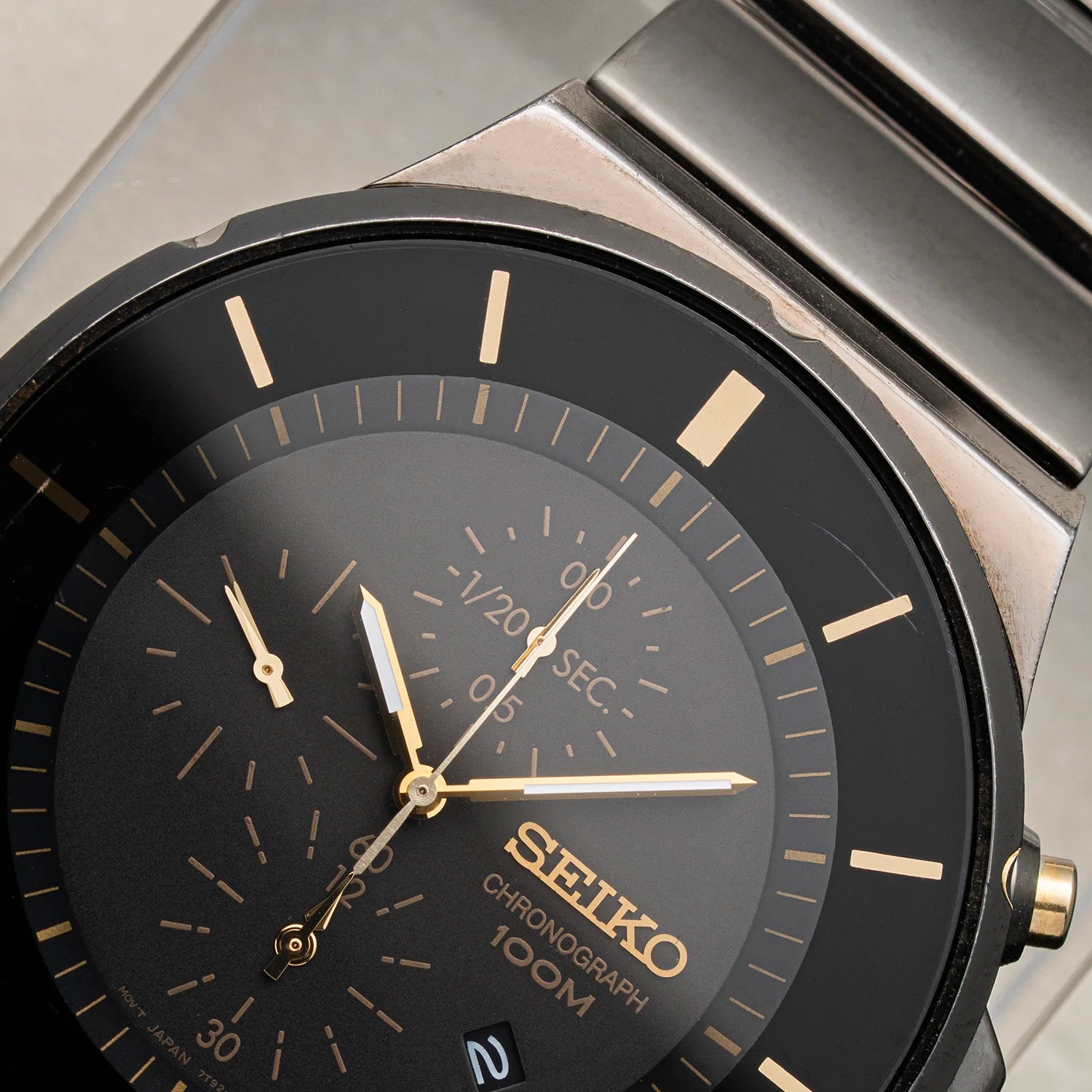 Close-up of a Seiko Chronograph, Ref. 7T92-0NGO watch with a black dial, gold-tone hands and markers, and a brushed silver-tone metal case and bracelet.
