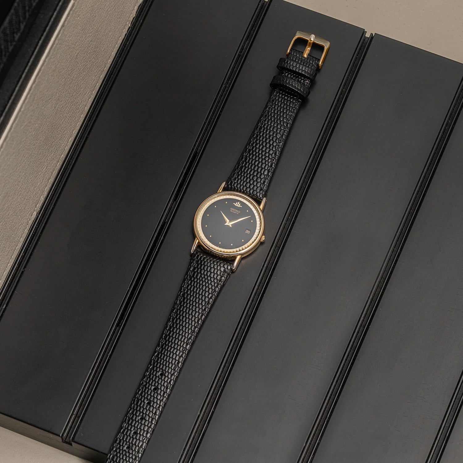 A luxury wristwatch Seiko, Ref. 5Y39-7010 with a gold-toned case, black dial, and textured black strap, presented diagonally on a black textured box.