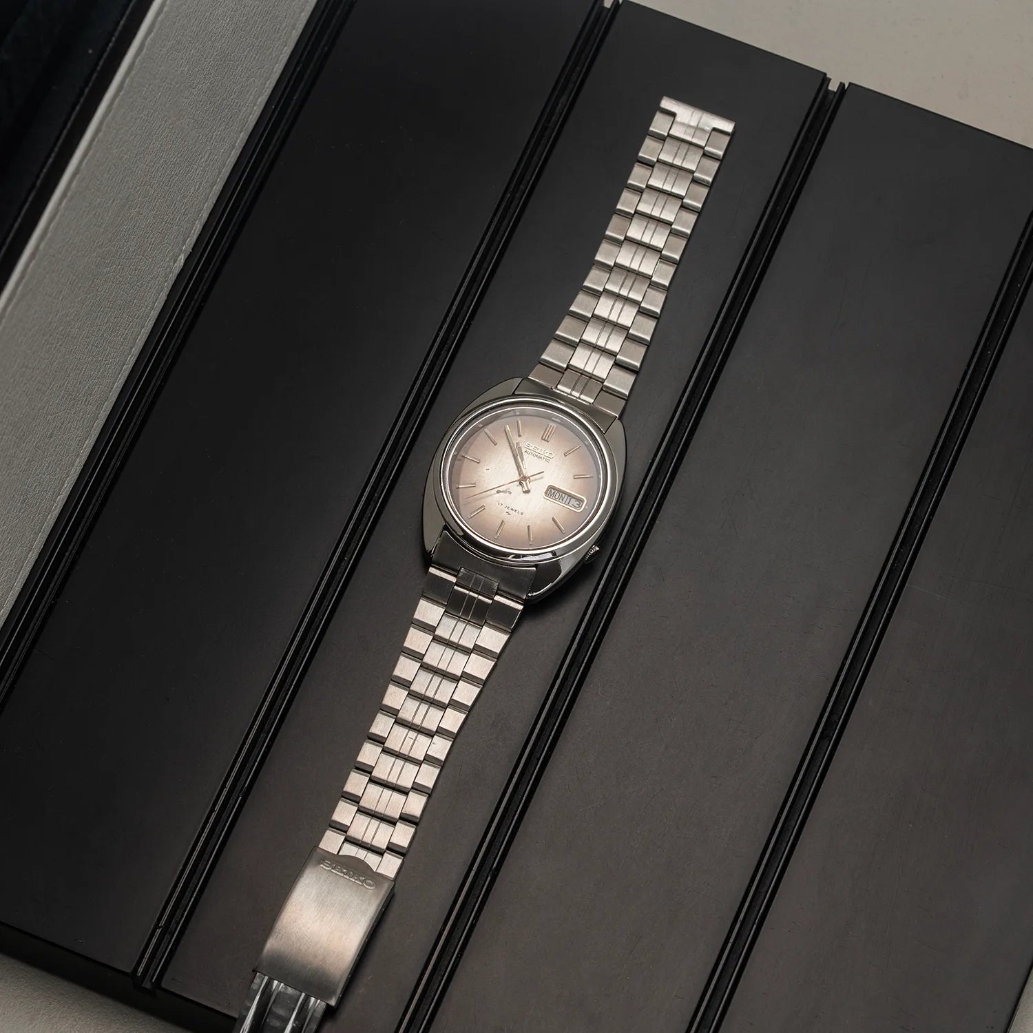 A silver-tone stainless steel wristwatch Seiko 7009-8081 with a matching link bracelet and a pale pink dial, displayed diagonally on a black presentation box.