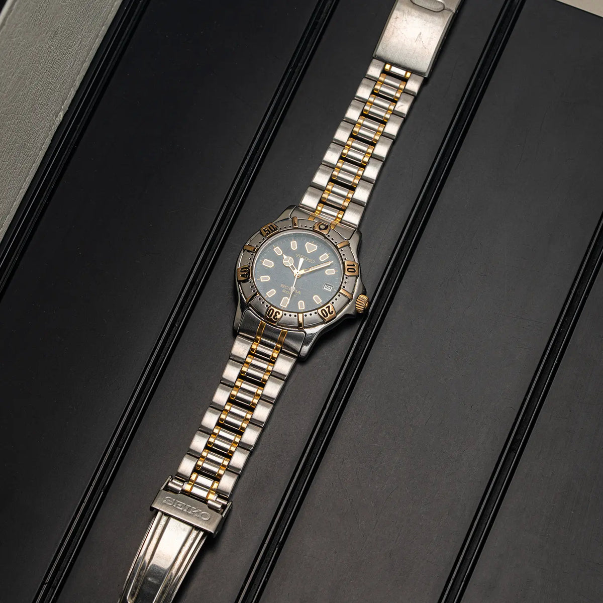 A two-tone Seiko Scuba 200M, Ref. 7N35-6020, Cal. 7N35, Diving, 1992 stainless steel and gold wristwatch with a blue dial, presented diagonally on a black textured background.