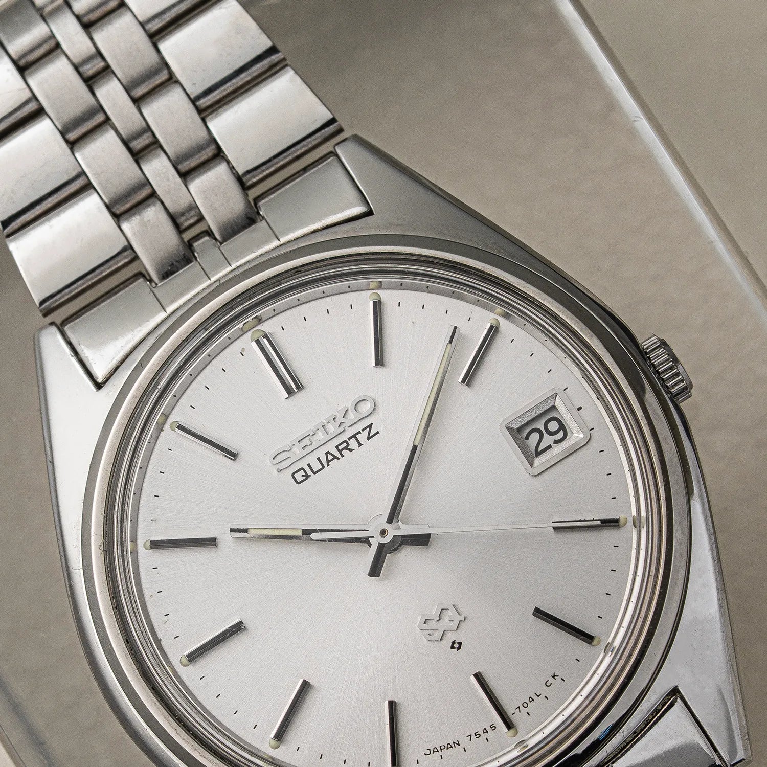 A close-up shot of a vintage Seiko SQ, Ref. 7545-7030 Quartz wristwatch with a silver stainless steel case and link bracelet, featuring a white dial with black markings and a date window showing '29'.