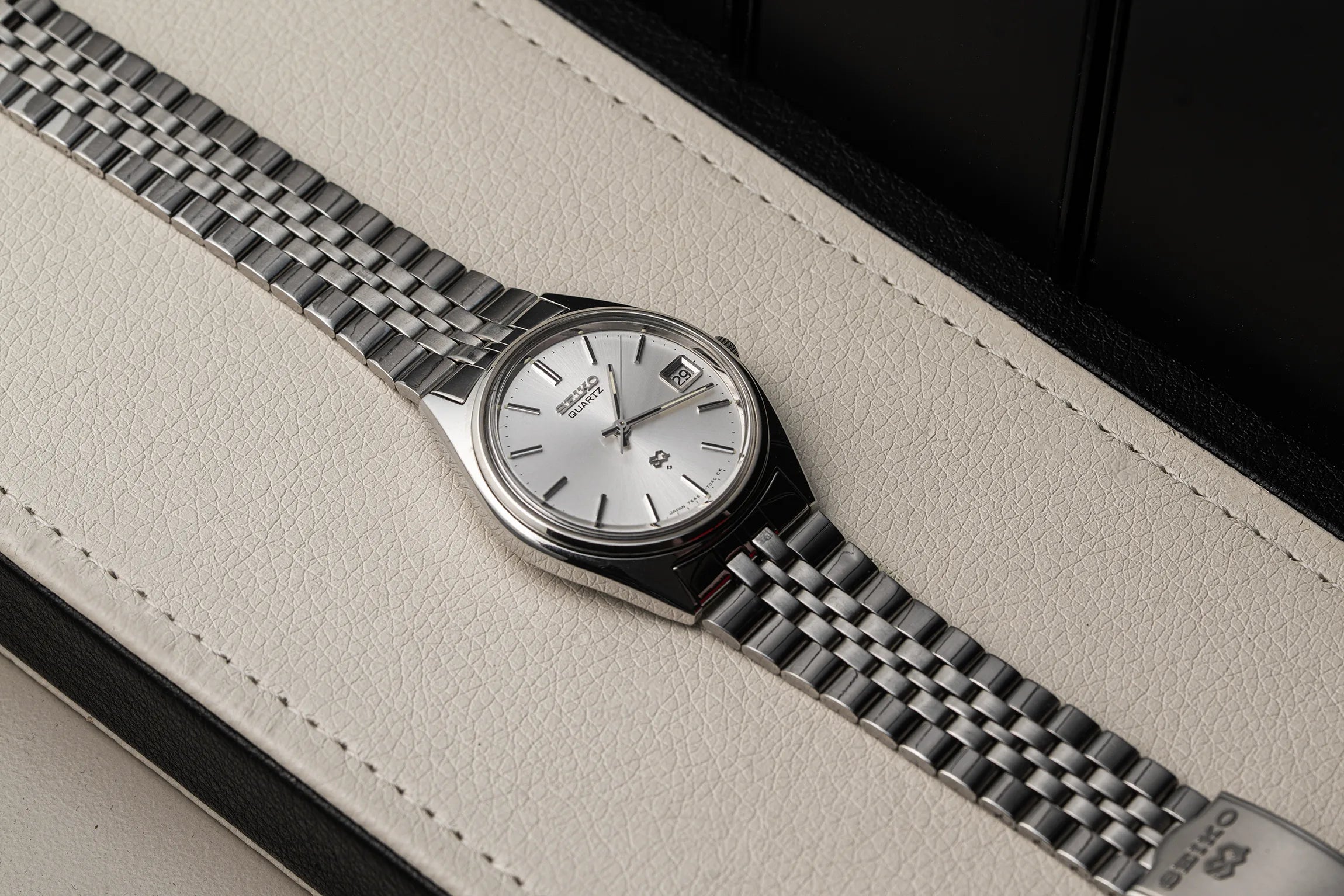 A stainless steel wristwatch Seiko SQ, Ref. 7545-7030 with a silver dial and matching metal bracelet, resting diagonally on a textured off-white leather surface with a dark background.