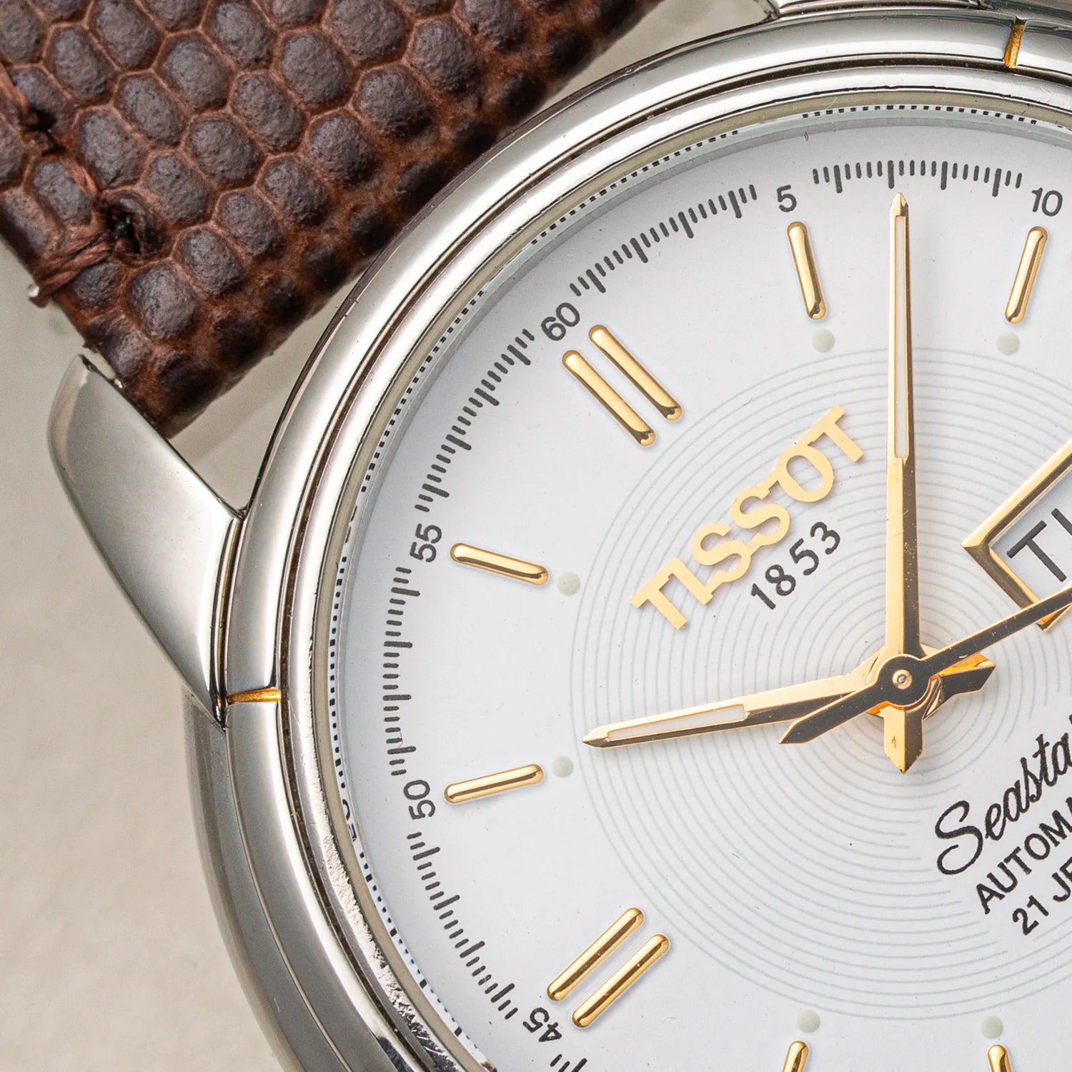 Close-up of a Tissot Seastar ETA 2846  Automatic watch with a silver-toned stainless steel case, white dial, gold-tone hands and markers, and a brown textured leather strap.
