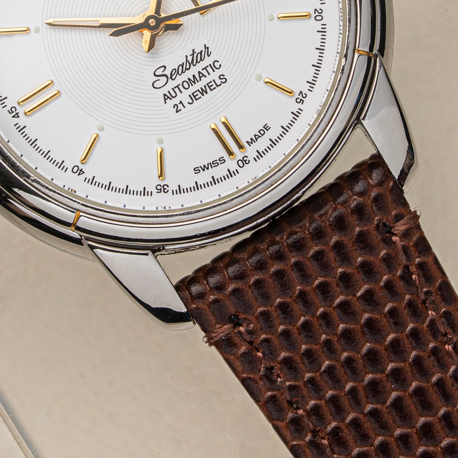 Close-up of a Tissot Seastar ETA 2846  Automatic 21 Jewels watch with a white dial, gold-tone markers and hands, and a textured brown leather strap on a light beige background.